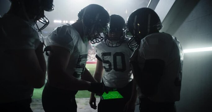 Team Captain Showing Game Strategy on a Tablet Computer Screen to a Group of American Football Players Before a Championship Match. Footballers Warming Up Before an Important Match