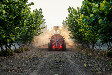 Rear view of tractor with big fan spraying orchard at rural countryside.