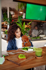 Woman eating at vegetarian cafe or restaurant with green smoothie and plant meal vegetables on...