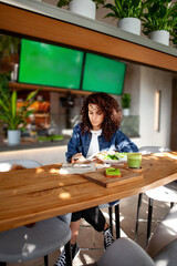Woman with curly hair seats at vegetarian cafe or restaurant with green smoothie and plant meal on...