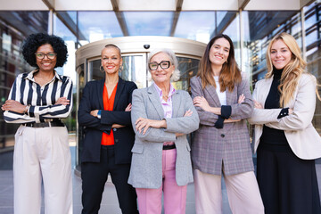 Five businesswomen standing side by side with their arms crossed looking at the camera smiling....