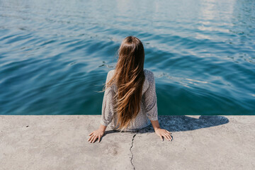 A woman is sitting on a ledge by a body of water, wearing a dress with a leopard print pattern. The scene is peaceful and serene, with the woman enjoying the view of the water and the surrounding area