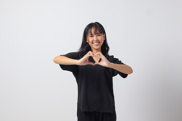 Portrait of attractive Asian woman in casual shirt speaks about own feelings, makes heart gesture over chest, expresses sympathy and love, smiles positively. Isolated image on white background