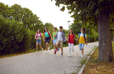 Happy boys and girls children walking among trees holding hands smiling wander along park path...