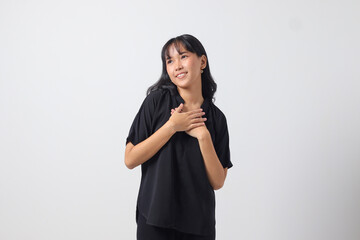 Portrait of attractive Asian woman in casual shirt placing hand on chest and feeling peaceful. Mental health day concept, expresses sympathy and love, smiles positively. Isolated on white background