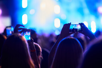 Concertgoers record live on smartphones, capturing stage lights, performance at music fest. Arms...
