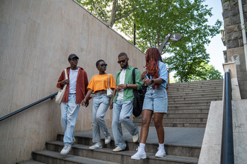 Serious excited four african american students girls and guys talks, go down stairs to underpass on...