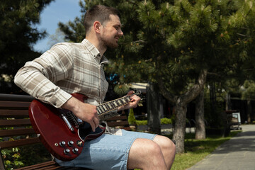 Attractive young guy playing guitar while sitting on a bench