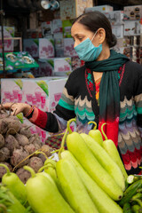 Indian mature woman wearing protective face mask and buying vegetables from outdoor market 