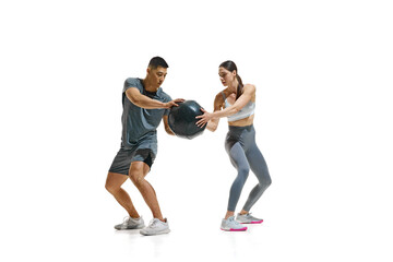 Sporty man and woman engaged in fitness exercise using large black medicine ball against white studio background. Concept of people in sport, healthy lifestyle, teamwork, motivation. Ad