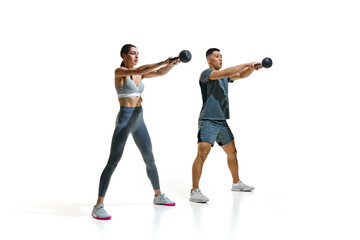 Obraz premium Young, athletic man and woman performing kettlebell exercise in motion against white studio background. Concept of people in sport, healthy lifestyle, teamwork, motivation. Ad
