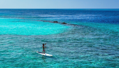 Happy Asian young man standing on a sup Surfing balancing on supboard paddling with water sea...
