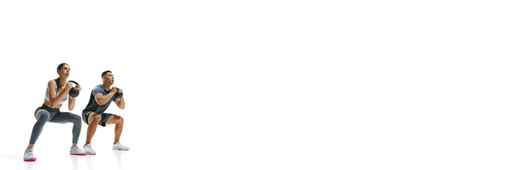 Banner. Man and woman mid-squat during kettlebell workout against white studio background with negative space. Concept of people in sport, healthy lifestyle, teamwork, motivation. Ad