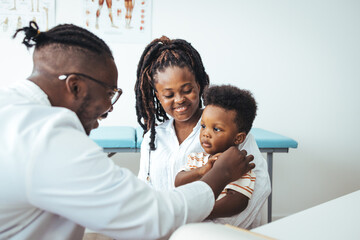 Smiling male pediatrician in white medical uniform holding clipboard, listening to young mother...