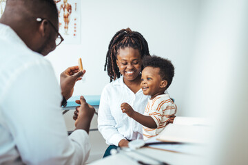 Smiling male pediatrician in white medical uniform holding clipboard, listening to young mother...