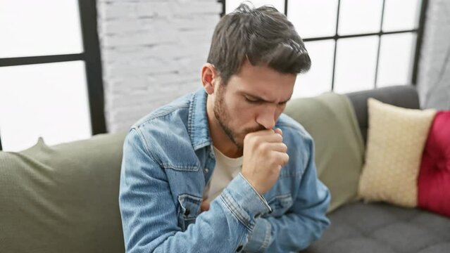 A young hispanic man coughing indoors, looking unwell in a casual setting, denoting sickness or allergies at home