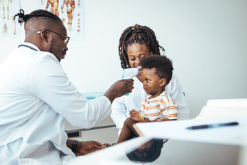 Happy young woman and her cute son looking at doctor and listening to his recommendations. Mother and baby son at a doctor´s appointment. Doctor measuring temperature of boy 