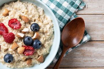 Oatmeal porridge with raspberries, blueberries and almonds in bowl on wooden table