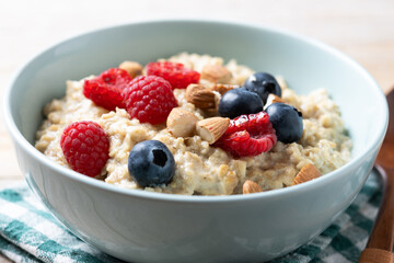 Oatmeal porridge with raspberries, blueberries and almonds in bowl on wooden table. Close up