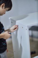 A young boy of 12 years old is learning to assemble furniture.