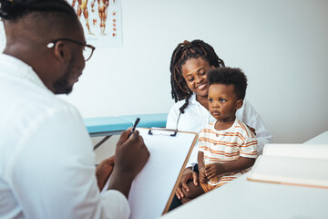 Smiling caring male pediatrician talk consult small boy patient at consultation in hospital with...