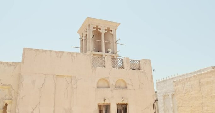 House in traditional Arabic architecture with wind tower. Traditional Arabic style building with windcatcher tower and palm leaves thatched roof. Old Dubai, UAE. Sounds call to prayer in Arabian city