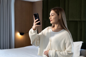 Beautiful long-haired girl taking selfie on smartphone in hotel room