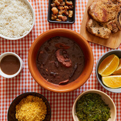 Bowl of feijoada surrounded by other preparations with farofa, cabbage, rice, steak, orange