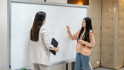 Two women are standing in front of a white board