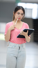 A woman in a pink shirt and jeans is holding a tablet and a pen