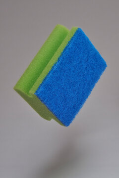 Close up green and blue cleaning sponge floating midair against gray background
