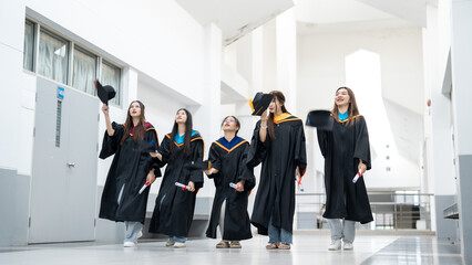 A group of five women in graduation gowns are walking down a hallway