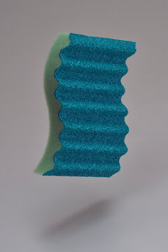 Rippled blue cleaning sponge floating midair against gray background
