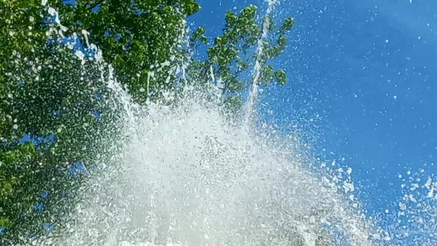 Water fountain in close-up, with the green background of tree leaves and the blue sky, crystal clear water makes a beautiful effect