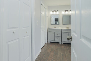 White and gray bathroom with a double sink, mirrors, and cabinets on each side