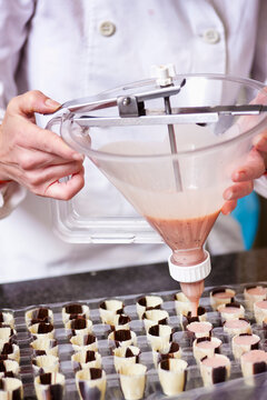 Close up of a chef's hands filling chocolate candy molds
