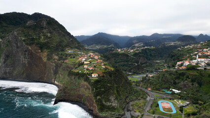 Aerial drone shot of a village on the green cliff on Madeira Island in Portugal. Blue ocean waves...