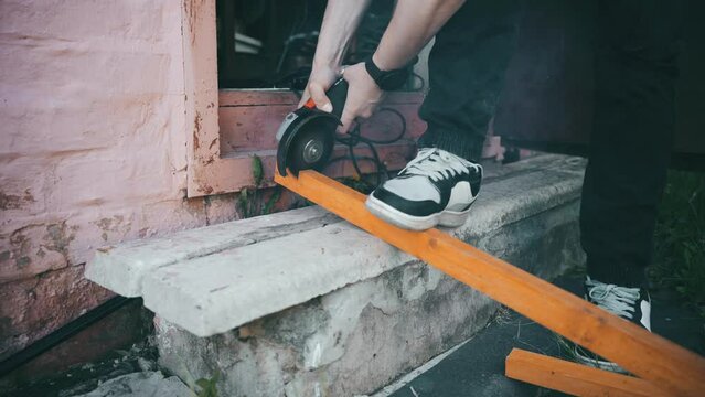 A man saws a thin board with a grinder. on the threshold of his workshop.