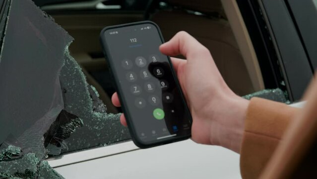 Hand swiftly dials 112 after noticing broken car window action for emergency help quick response required. Fingers quickly press 112 upon seeing shattered vehicle glass emergency assistance.