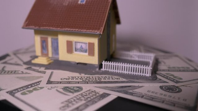 Normal footage of a house placed on a hundred U.S. dollar bills.