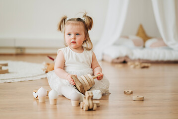 Cute beautiful girl baby sitting on the floor in the children's room and playing in eco wooden toys...