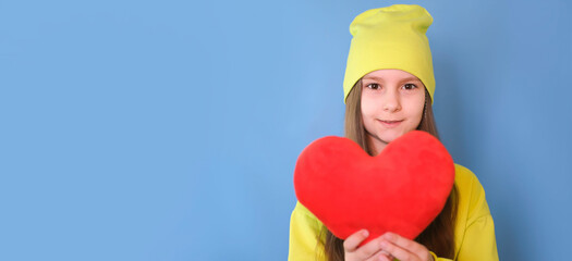 Beautiful little girl smiling at camera holding toy heart on blue background. Love and Valentine's...
