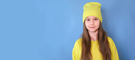 Banner. Portrait of happy cute girl smiling sweetly at camera in a green hat on blue background.