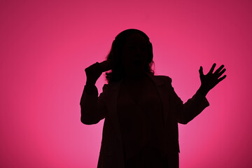 Silhouettes of mature woman singing with microphone against pink background