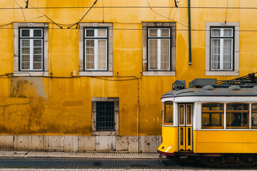Yellow tram moving past yellow building in Lisbon, Portugal 