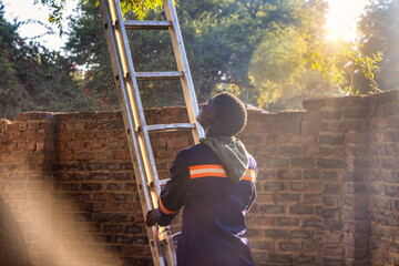 african worker climbing a stepladder in the yard, dust in the air at sunset