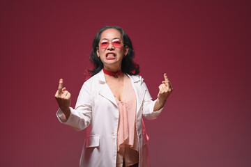 Studio shot of crazy funny mature woman showing middle finger gesture over red background