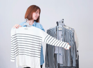 Beautiful young woman and a stand with different T-shirts and shirts on a gray background