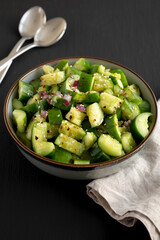 Homemade Smashed Cucumber Salad in a Bowl on a black background, side view.
