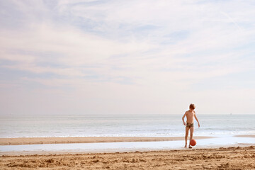 Boy is playing with ball on the beach with copy space. Playful casual family enjoying. Summer